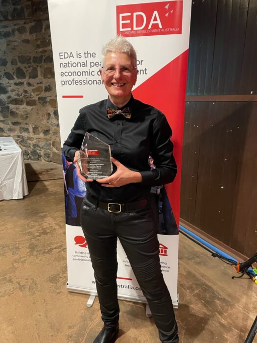 Sue Arlidge holding EDA award in front of EDA banner at award ceremony.