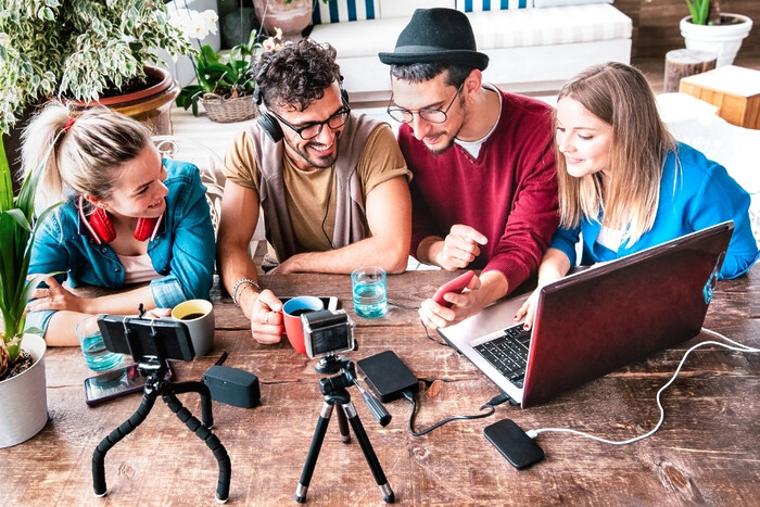Group of 4 people sitting around table with laptop and recording devices.