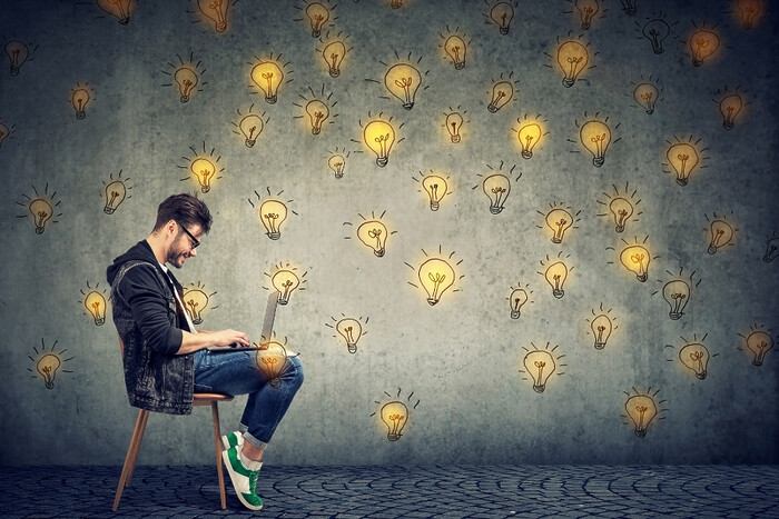 Man sitting on chair with laptop open, surrounded by idea bulbs.